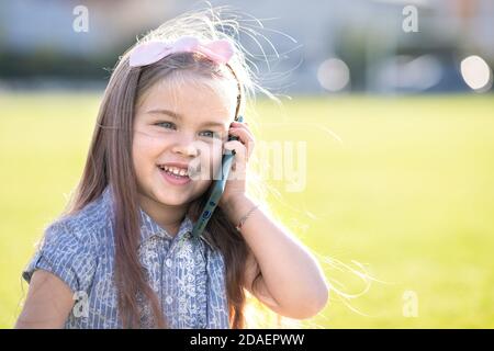 Pretty little child girl speaking on mobile phone smiling happily outdoors in summer. Stock Photo