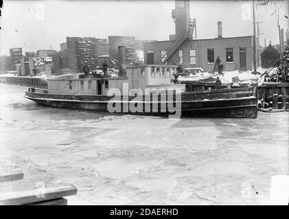 Fireboat, the Swenie, with three men standing on its decks, docked on the Chicago River in front of an industrial building with boards stacked nearby Stock Photo