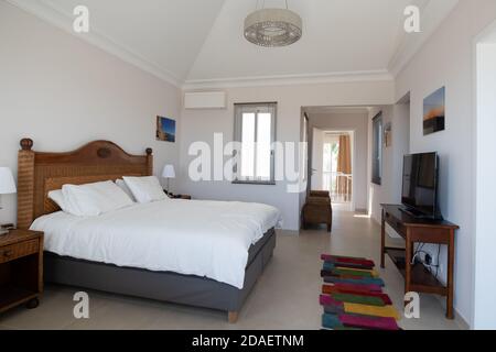 Master bedroom with wooden furniture and white bedding in a light and airy room in renovated holiday villa Stock Photo