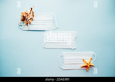 Medical masks and seashells on a blue background. Protection from COVID-19 concept. Flatlay. Top view. Stock Photo