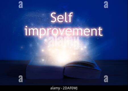 Open book with self improvement inscription. Light coming from open book with words self improvement. Stock Photo