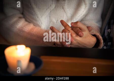 Close up of couple sitting in a cafe and holding hands together behind a wooden table with a burning candle. Love story concept Stock Photo