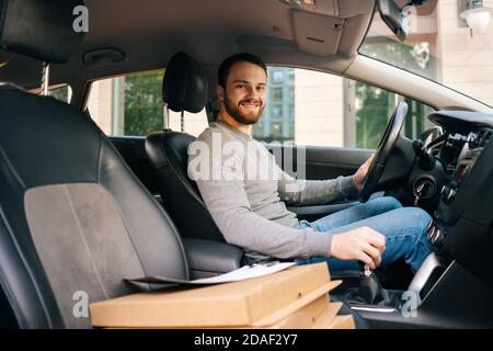 Professional bearded delivery man wearing casual clothes driving car delivered hot pizza to customer Stock Photo