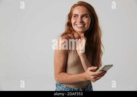 Image of beautiful positive cheery redhead woman with freckles using mobile phone isolated over white wall background Stock Photo