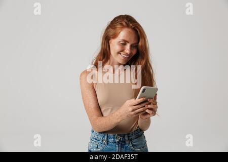 Image of beautiful smiling happy redhead woman with freckles using mobile phone isolated over white wall background Stock Photo