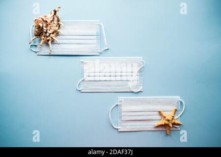 Medical masks and seashells on a blue background. Protection from COVID-19 concept. Flatlay. Top view. Stock Photo
