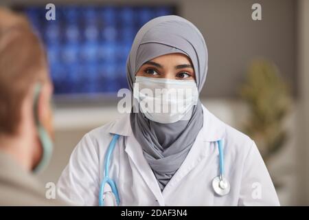 Portrait of muslim doctor in protective mask looking at her patient while they sitting at hospital Stock Photo
