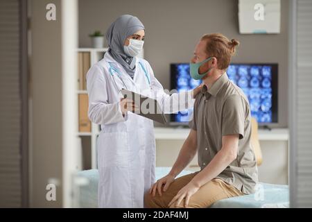 Female doctor in protective mask using digital tablet treating the patient at hospital Stock Photo