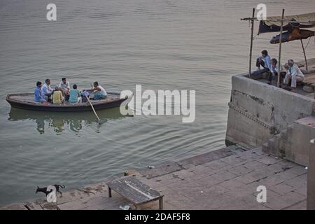 Varanasi, India, December 2015.  People in a ghat look at a boat sailing on the Ganges River. Stock Photo