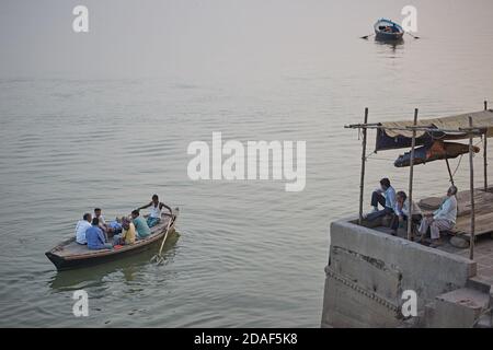 Varanasi, India, December 2015.  People in a ghat look at a boat sailing on the Ganges River. Stock Photo