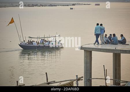 Varanasi, India, December 2015.  People in a ghat look at a boat sailing on the Ganges River. Stock Photo