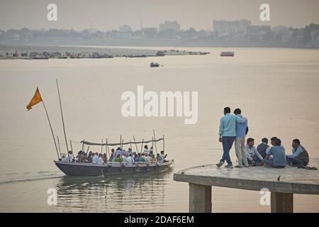 Varanasi, India, December 2015.  People in a ghat look at a boat sailing on the Ganges River. Stock Photo