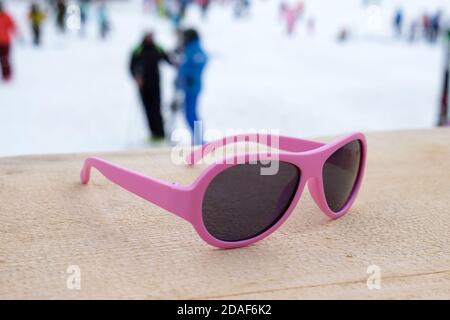Pink-rimmed sunglasses on wooden slope in apres ski bar or cafe, with ski slope in background. Concept of winter sports, leisure, recreation, relaxati Stock Photo