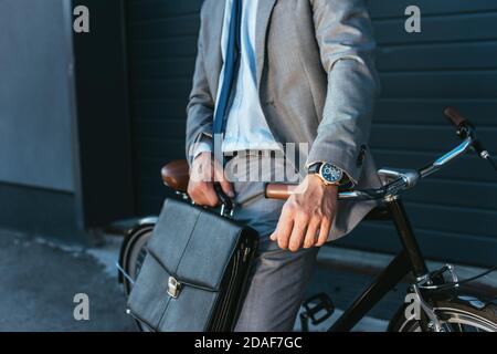Cropped view of businessman in suit holding briefcase near bicycle outdoors Stock Photo