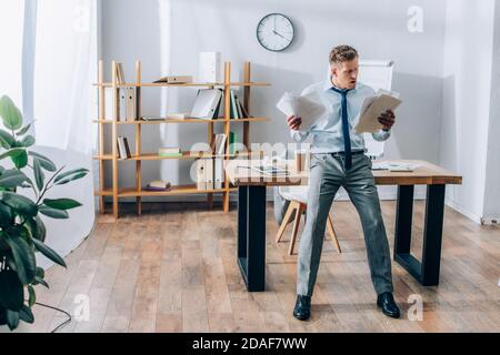 Confused businessman looking at papers near digital tablet and coffee to go on working table Stock Photo