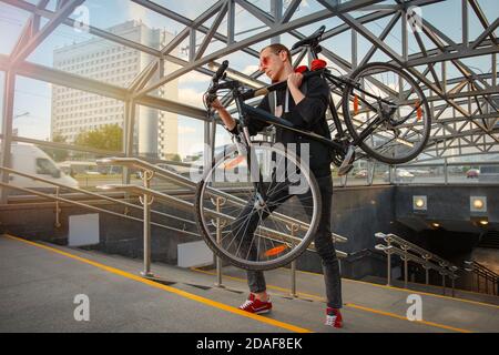 A young biker climbs the stairs of the underpass and carries a bicycle on his shoulder. Stock Photo