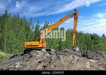 Yellow tracked excavator at work site on a heap of earth on a beautiful day of summer. Stock Photo