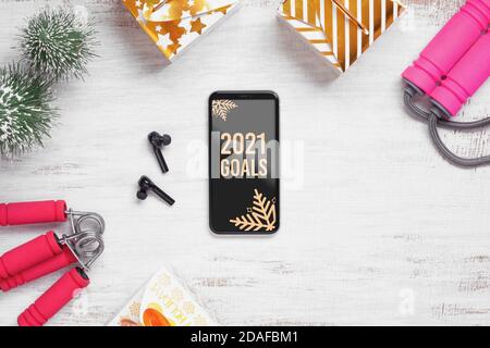 2021 New Year resolutions  healthy goals background concept. 2021 Goals text on mobile phone on table with jump rope, wireless earphone,  and Christma Stock Photo