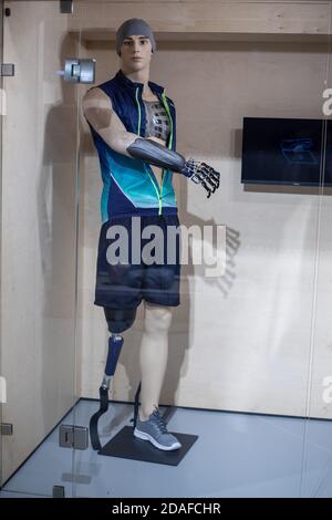 A mannequin in the form of a young man in sportswear with a prosthetic arm and leg behind glass. Demonstration of new technologies in prosthetics Stock Photo