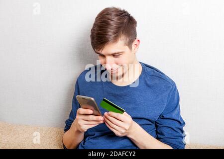 Young Man with a Phone and a Bank Card by the Wall in the Room Stock Photo