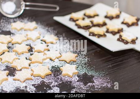 In the time before Christmas, cookies are baked at home in a star shape. Shortcrust pastry stars are covered with chocolate and sprinkled with powdere Stock Photo