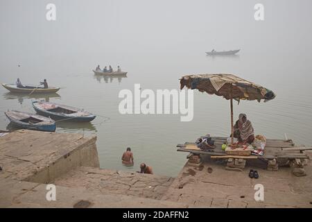 Varanasi, India, December 2015. People in a Ganges river ghat with rowboats in the background on a foggy day. Stock Photo