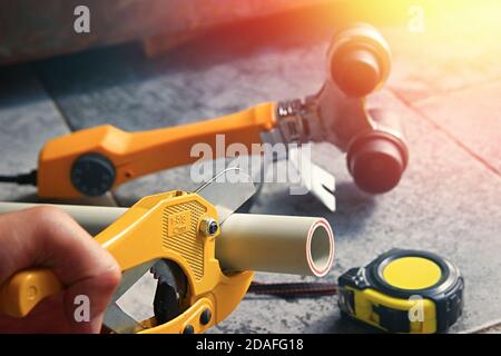 Close-up of hand with yellow scissors cut pipes for heating, or water supply. Polypropylene or pvc mounting system. Stock Photo