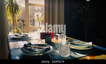 Table setting for romantic breakfast in the morning sun through a window. Shadows and sunbeams in dark room. Stock Photo