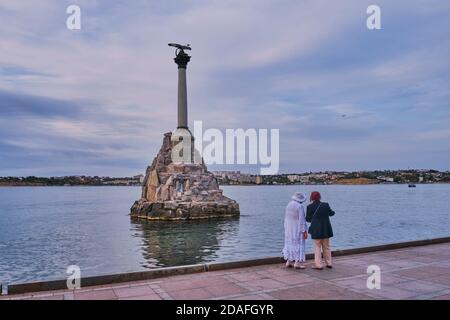 Sevastopol, Russia - September 28, 2020: Two elderly women friends are walking along the seaside promenade at sunset. The Monument to the Sunken Ships Stock Photo