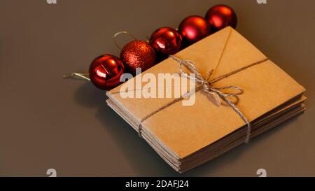 Christmas composition. Craft envelopes and Christmas red balls with copy space. Stack of letters tied with twine on brown background Stock Photo