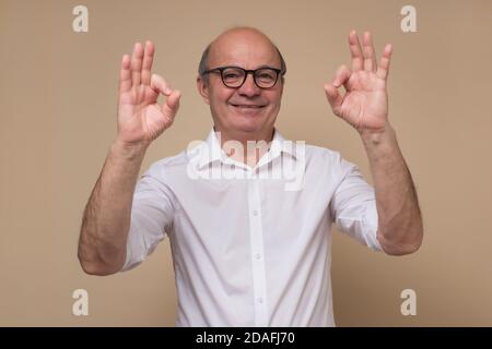 Happy mature bald man in glasses doing ok gesture. Stock Photo