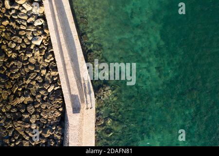 Aerial view of two people casting long shadows on the walkway to the lighthouse in the city of Chania, Crete, Greece Stock Photo