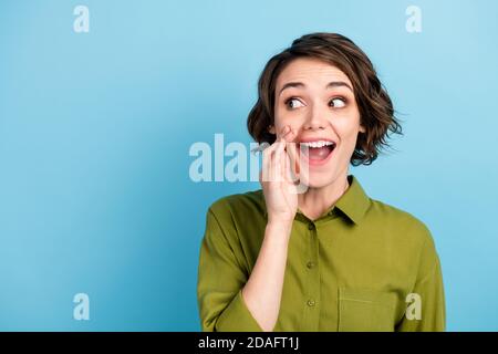 Photo portrait of young pretty girl with short hair telling secret information rumouring gossiping wearing green shirt isolated on blue color Stock Photo