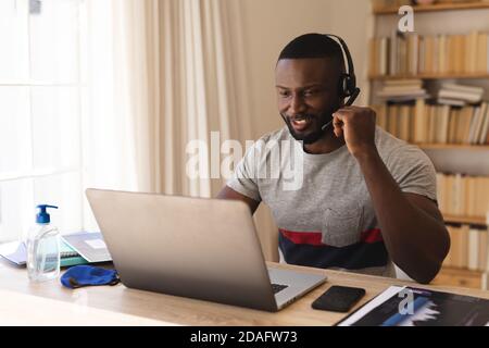 African american man using phone headset while having a video chat on laptop while working from home Stock Photo