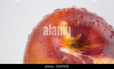 A drop of water flows down a fresh juicy peach. Fresh organic Peach covered with dew drops. Fresh juicy peaches on a white plate. Stock Photo