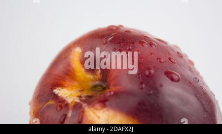 A drop of water flows down a fresh juicy peach. Fresh organic Peach covered with dew drops. Fresh juicy peaches on a white plate. Stock Photo