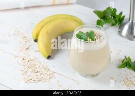 Banana milkshake with oat milk. On the wooden rustic white table. In the cocktail are whole grains of oat and mint for freshness. Morning smoothie. Stock Photo