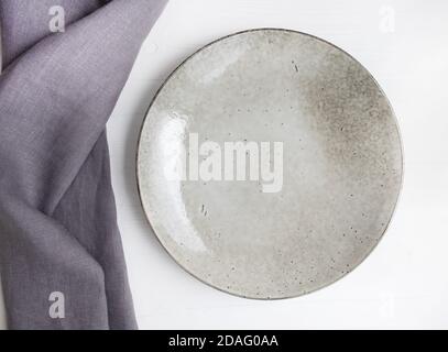 Gray linen towel and ceramic plate on a white wooden background. Serving. Stock Photo