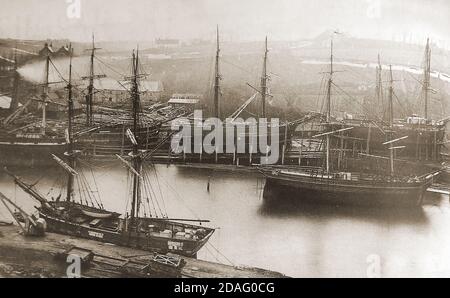 A rare & unusual old photograph showing sailing ships being built or repaired at the Whitehall shipyard on the river Esk at , Whitby, North Yorkshire (UK) during the Victorian period. White Hall, or Whitehall  (still standing in 2020) was the home of the shipyard owner, Thomas Turbull. The two gable ends of the building (top left) can be seen in the picture. A collier (coal ship) selling coal to the public is moored on the other side of the river close to where the Co-op store carpark and marina are situated today (2020) Stock Photo