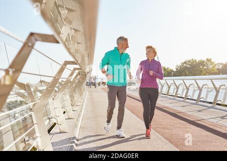 Morning activity. Full length shot of active mature family couple in sportswear smiling at each other while jogging together on a sunny morning Stock Photo