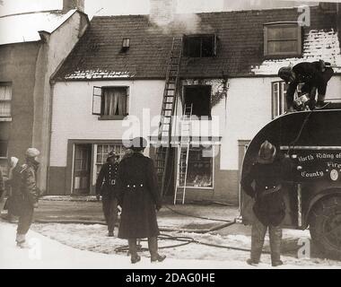 A vintage photograph showing a North Riding of Yorkshire (UK) fire crew, tackling a blaze above Paylor's fruit shop, Church Street, Whitby, North Yorkshire with snow on the ground. Stock Photo