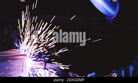 worker wears welder protective mask while welding metal with sparks in dark background. Stock Photo