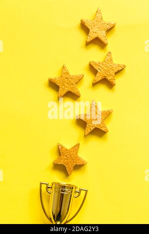 Simply flat lay design winner or champion gold trophy cup and 5 stars rating isolated on yellow background. Victory first place of competition. Winning or success concept. Top view copy space Stock Photo