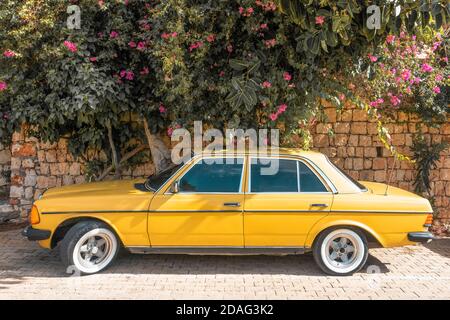 Mercedes benz w123. Yellow hipster Mercedes benz w123 against the background of the wall and bright flowers in summer. Stock Photo