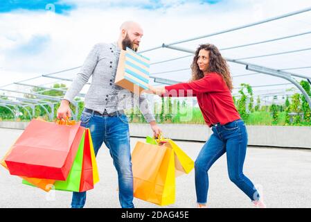 couple of a bearded bald man and a brunette curly woman making shopping during black friday sales. happy boy and a girl making fun of purchasing Stock Photo