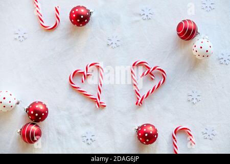 Heart shapes made from candy canes, red white spotted trinkets on white textile. Hand hold heart. Stock Photo