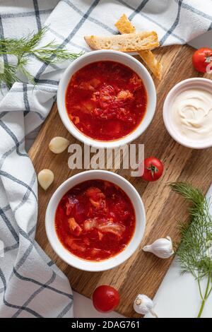 Homemade Traditional Ukrainian beet soup with fresh green dill. Russian borscht in bowl of tomatoes, sour cream, and mushrooms on white background. Top view. Stock Photo