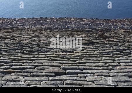 Looking down a sloping reservoir stone wall, a full frame abstract texture image is formed. Deep blue water ripples form good copy space. Stock Photo
