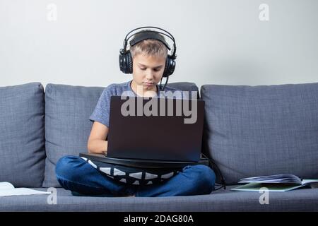 Child with headphones using laptop computer at home for online learning, homework, playing video games Stock Photo