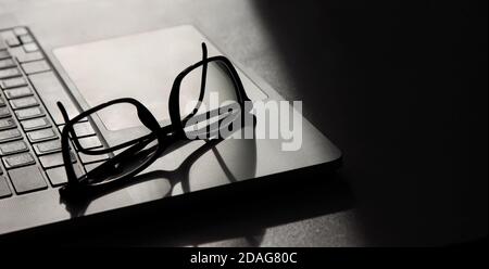 shadow falls on an open laptop on which reading glasses lie Stock Photo
